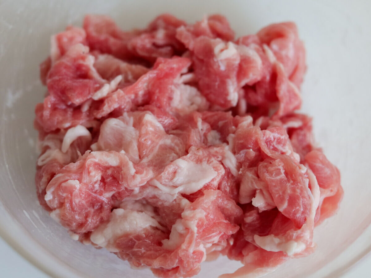 透明なボウルに入った、下味を揉み込んだ豚こま切れ肉のアップ 透明なボウルに入った、下味を揉み込んだ豚こま切れ肉のアップ