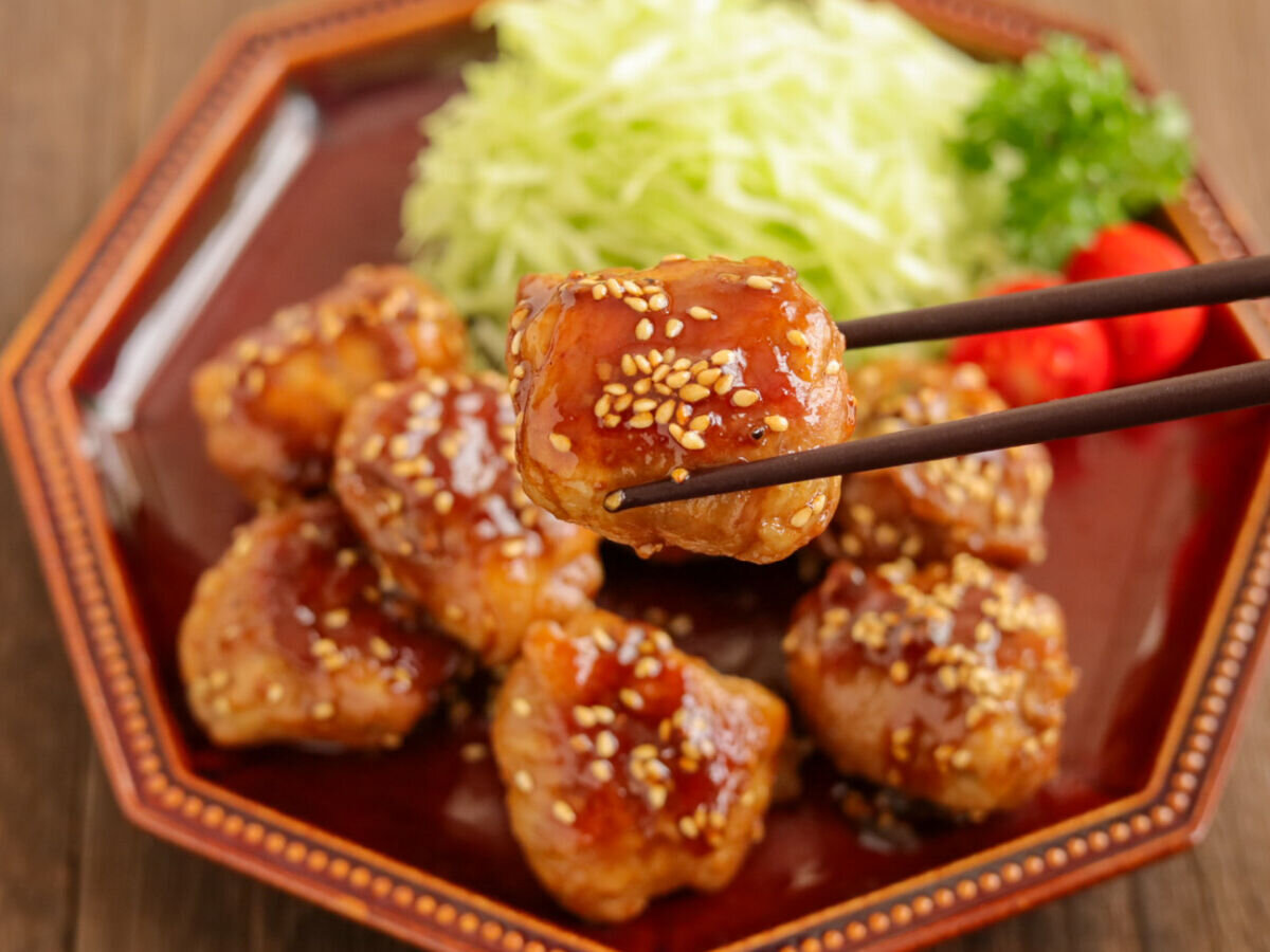 箸で持ち上げられた、白いりごまが振られた豚こまボールの照り焼き 箸で持ち上げられた、白いりごまが振られた豚こまボールの照り焼き
