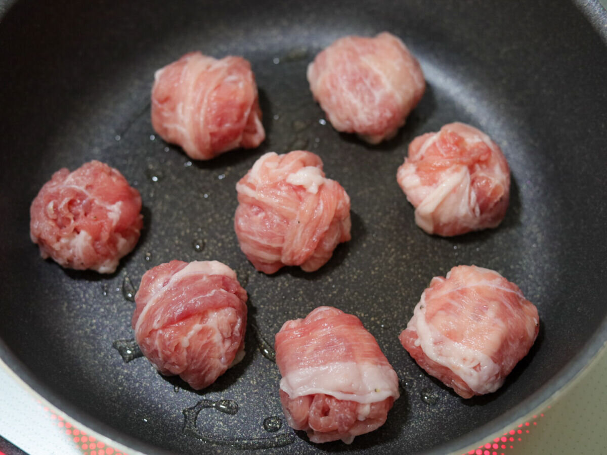 フライパンに油を熱し、丸めた豚こまボールを並べて焼いている様子 フライパンに油を熱し、丸めた豚こまボールを並べて焼いている様子