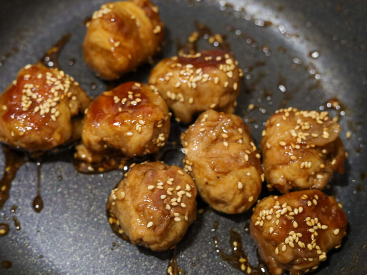 フライパンで照り焼きのタレが絡み、白いりごまが振られた豚こまボール フライパンで照り焼きのタレが絡み、白いりごまが振られた豚こまボール