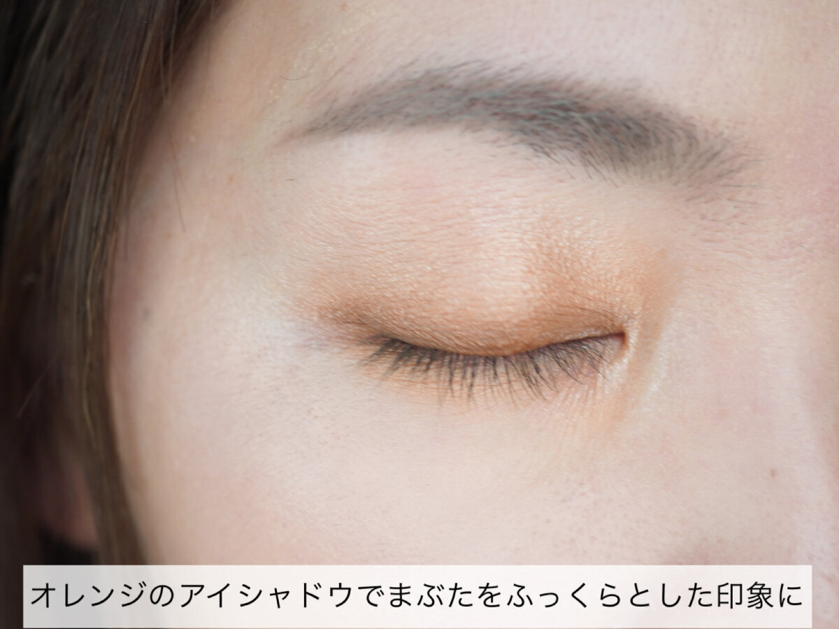 女性の閉じた目元アップ。オレンジ系アイシャドウが塗られている。
