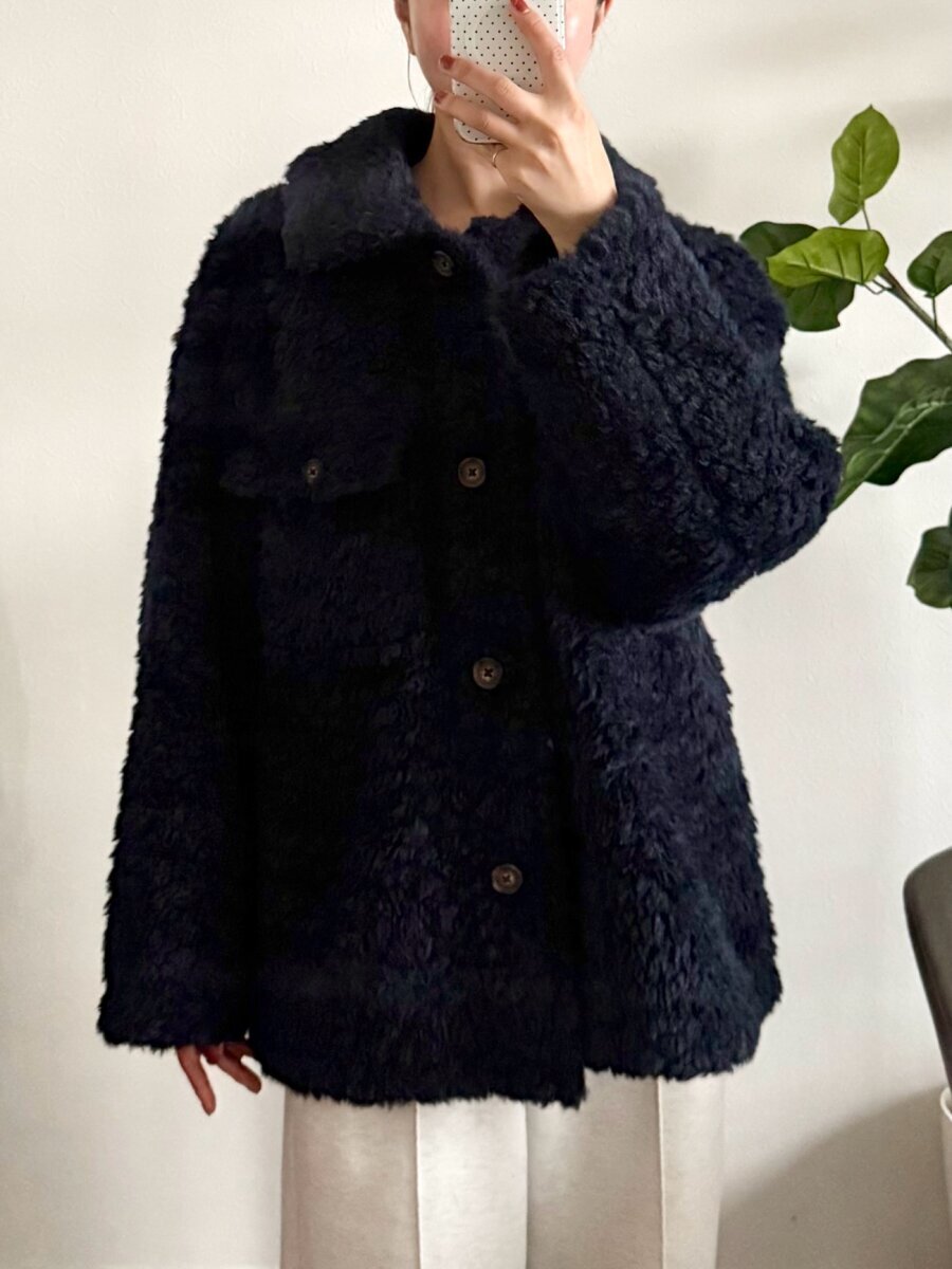一名身穿海軍藍抓絨外套的女子正在用智慧型手機自拍。 ネイビーのボアジャケットを着用した女性が、スマホで自撮りしている