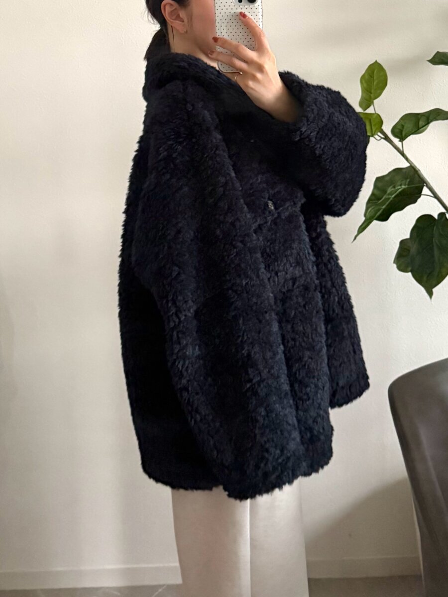 一名身穿海軍藍抓絨外套的女子正在用智慧型手機側身自拍。 ネイビーのボアジャケットを着用した女性が、横向きでスマホで自撮りしている