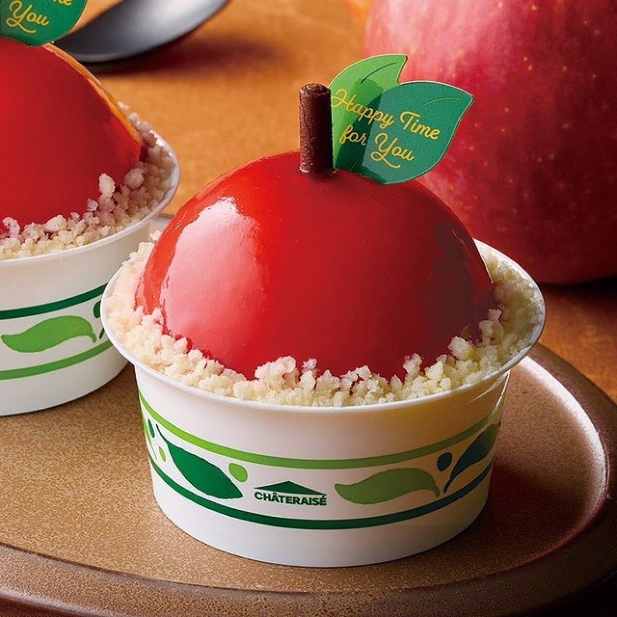 赤いりんごの形をしたケーキが白いカップに入っている。白いクランチと緑の葉っぱの飾りが特徴。