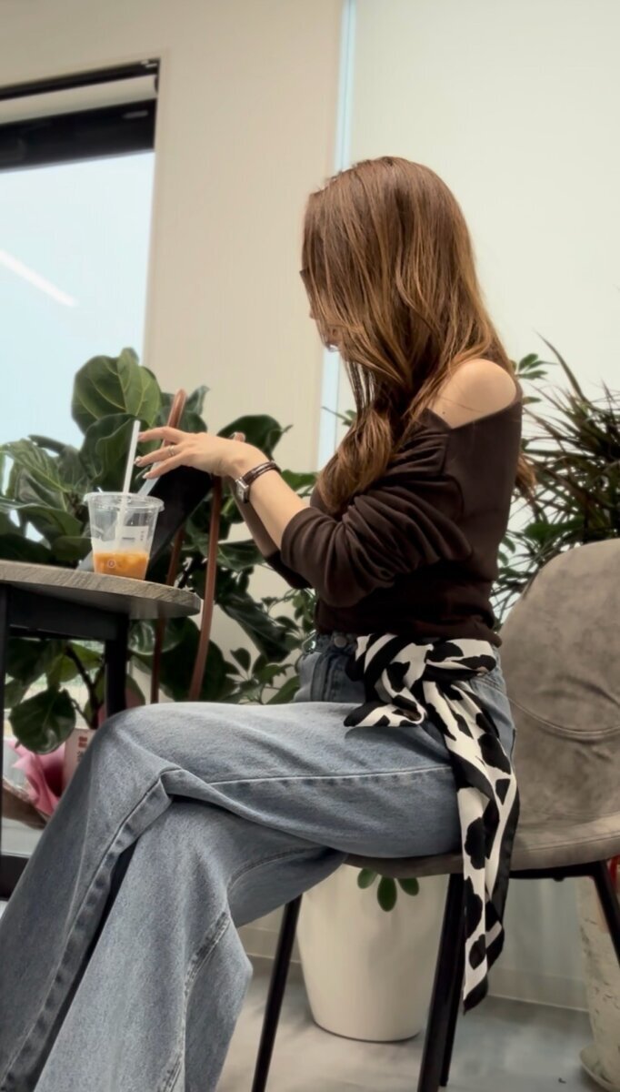 カフェで椅子に座りドリンクを飲みながら寛ぐブラウントップス姿の女性