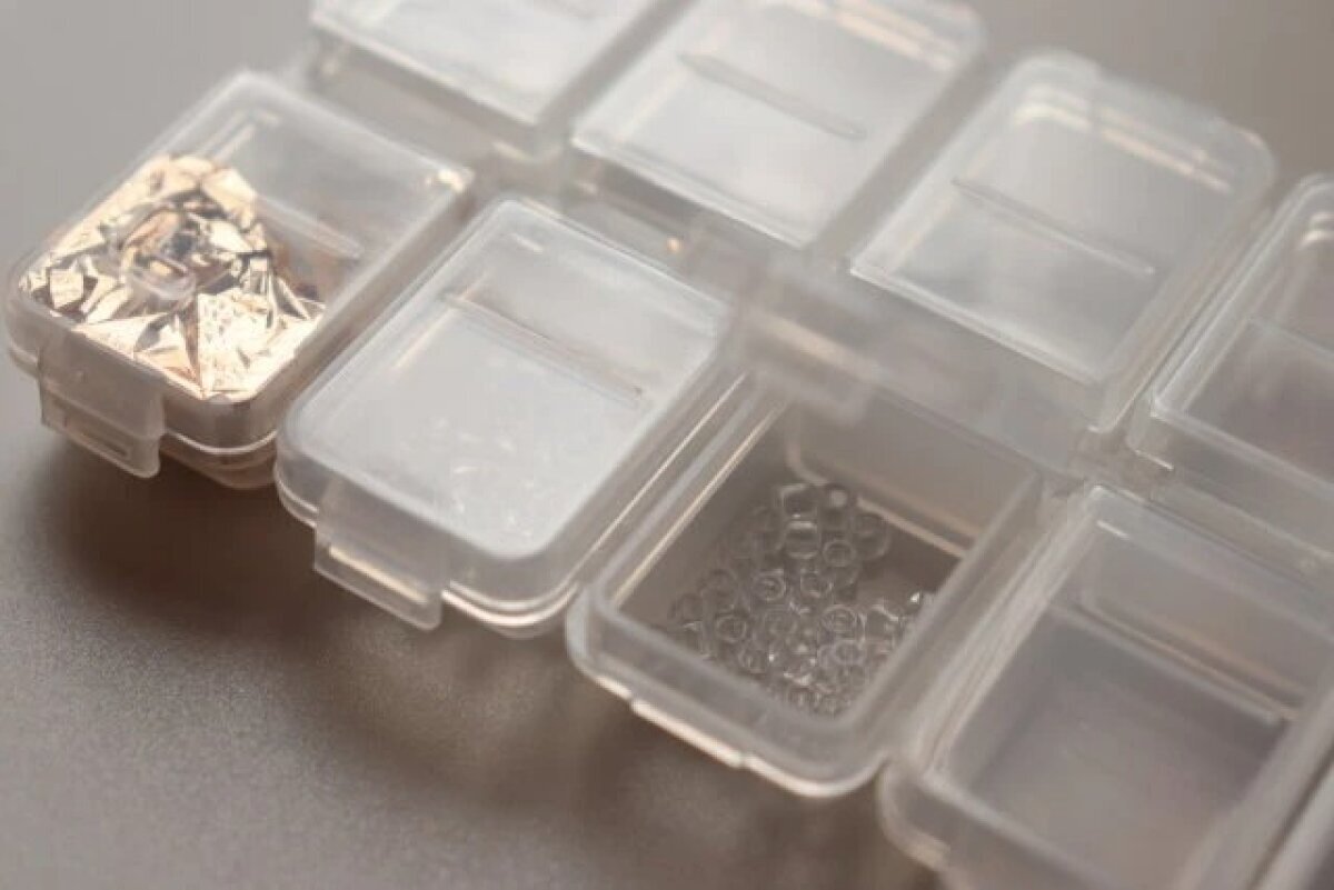 半透明のネイルパーツ収納ケースに、金箔やクリアなビーズなどのパーツが入っている
