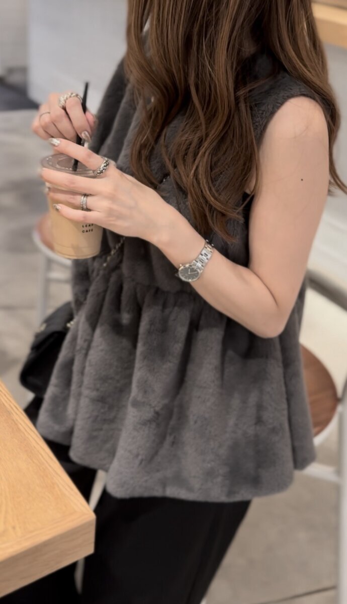 身穿褶邊皮草背心、手持飲料的女士。 ペプラムシルエットのファーベストを着てドリンクを持つ女性