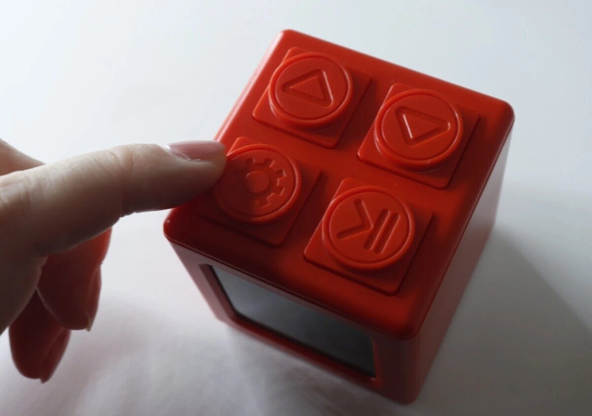 赤いブロック型デジタルタイマー時計の操作ボタンを指で押している様子