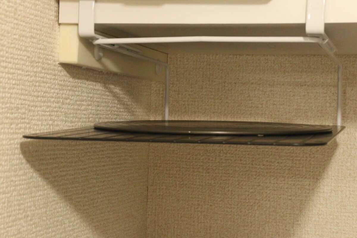 一塊黑色圓形砧板存放在吊櫃下方的架子上。 吊り戸棚の下に設置されたラックに黒い丸いまな板が収納されている