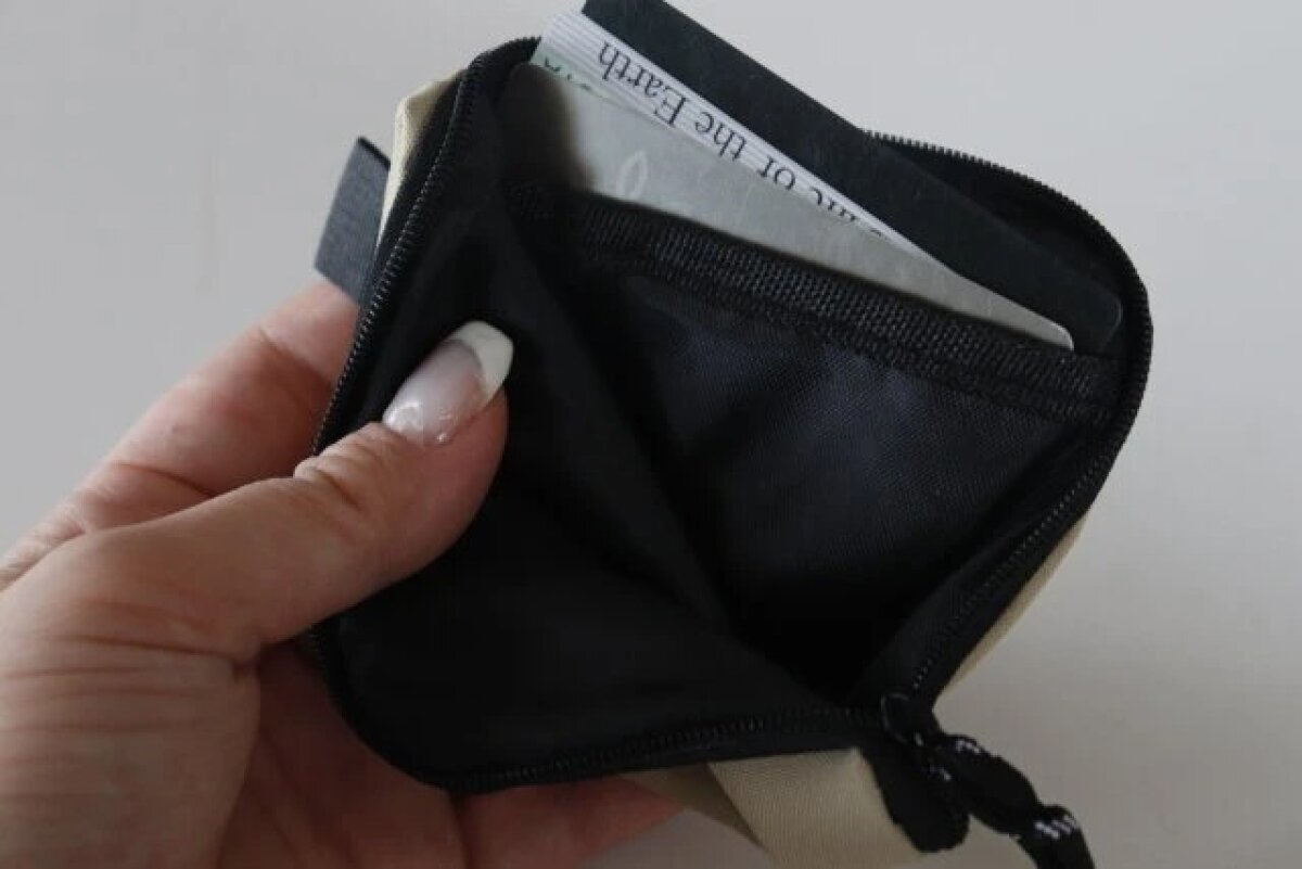 女性がベージュのコインケースのファスナーを開け、中にカードが数枚入っている