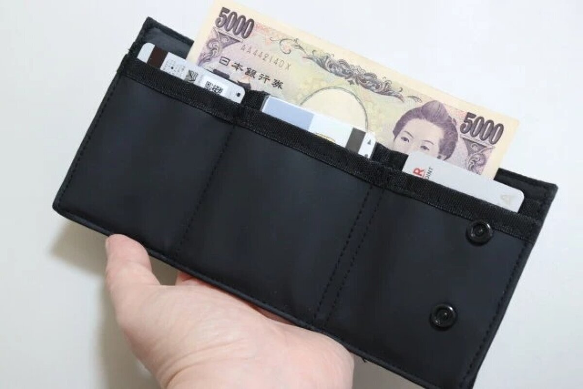 黒い三つ折り財布を開き、お札とカードが収納されている様子