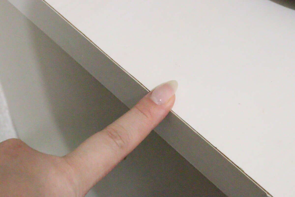 圖片顯示有人用食指指向一件白色家具的頂部和側角。這是一個可能的安裝位置範例。 白い家具の天板と側面の角を人差し指で指し示している様子。設置場所の例。