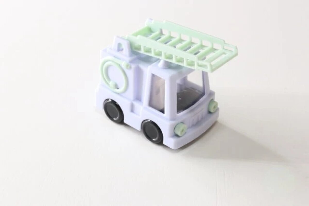一個粉彩色的消防車形狀的削鉛筆機略微斜放在前面。 パステルカラーの消防車型鉛筆削りが、正面から少し斜めに置かれている