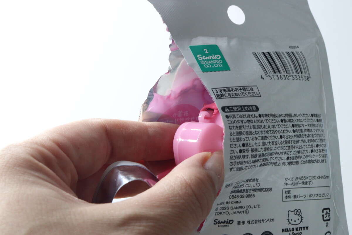 一位女士正在打開一個美樂蒂鑰匙圈的包裝。 女性がマイメロディキーホルダーのパッケージを開封する様子