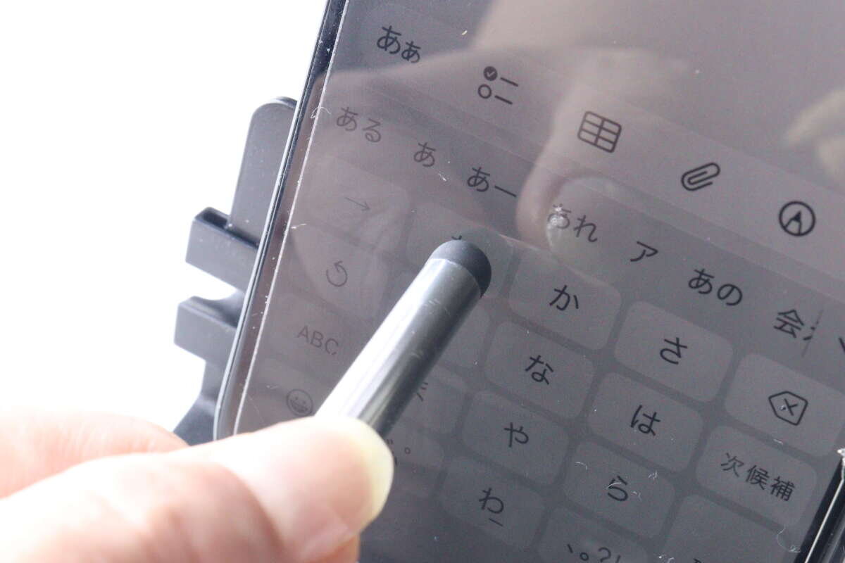 圖片顯示有人正在使用銀色觸控筆操作智慧型手機螢幕上的鍵盤。 銀色のタッチペンを使って、スマートフォン画面のキーボードを操作している様子。
