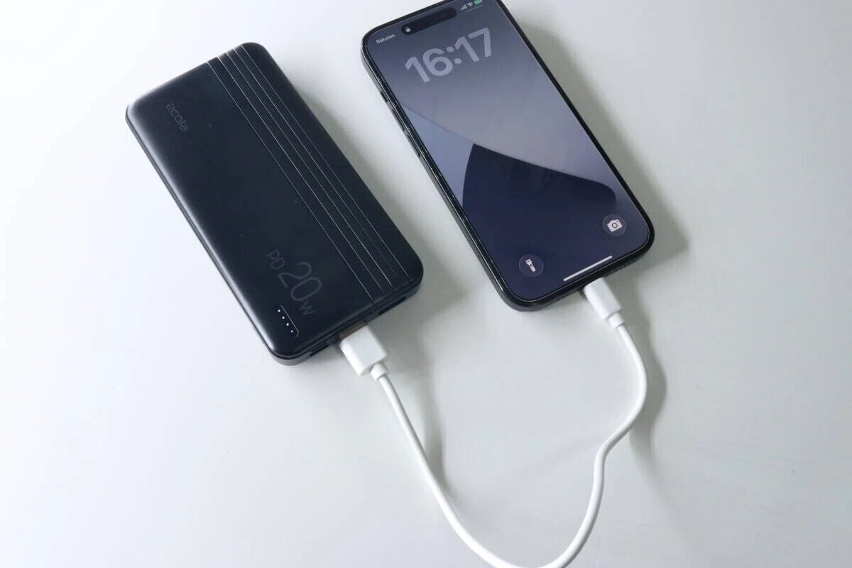 一塊黑色行動電源和智慧型手機透過白色充電線連接並正在充電。 黒いモバイルバッテリーとスマートフォンが白い充電ケーブルで接続され充電中