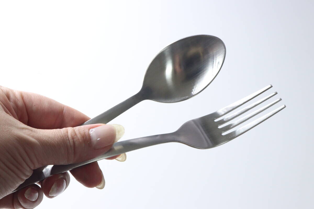一位女士的手拿著疊放在一起的不銹鋼甜點勺和甜點叉。 女性の手がステンレス製デザートスプーンとデザートフォークを重ねて持っている