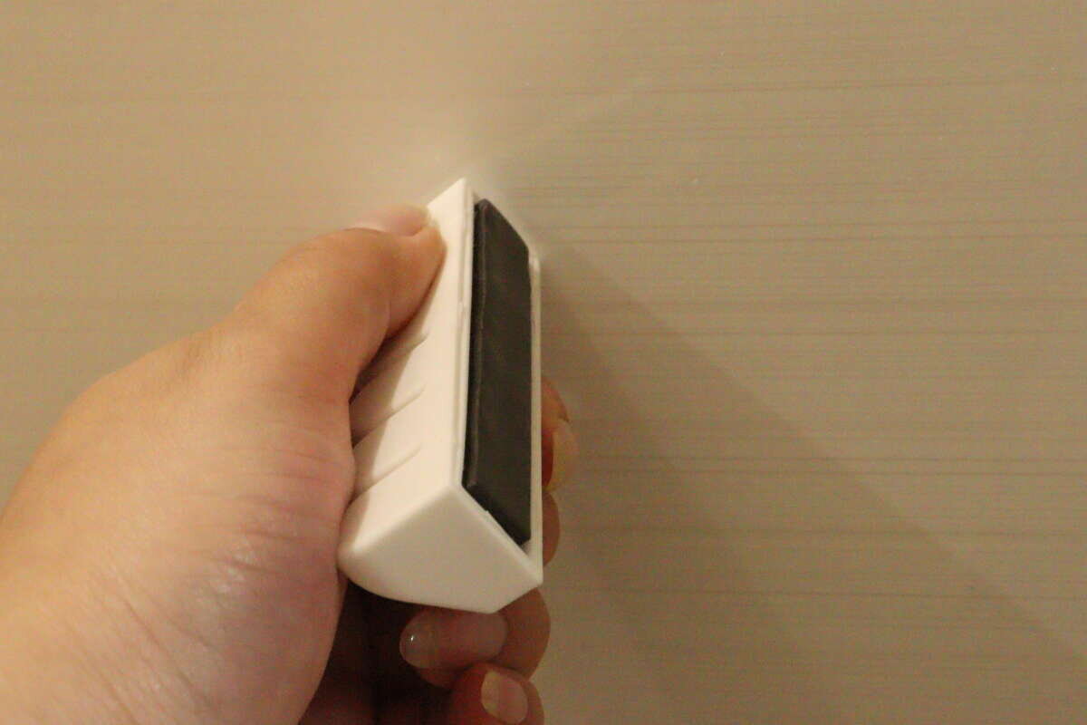一名女子正用手將白色晾衣網架的磁性面按在牆上,試圖將其安裝好。 女性の手が白い洗濯ネットホルダーを壁に設置しようと、磁石面を壁に当てている