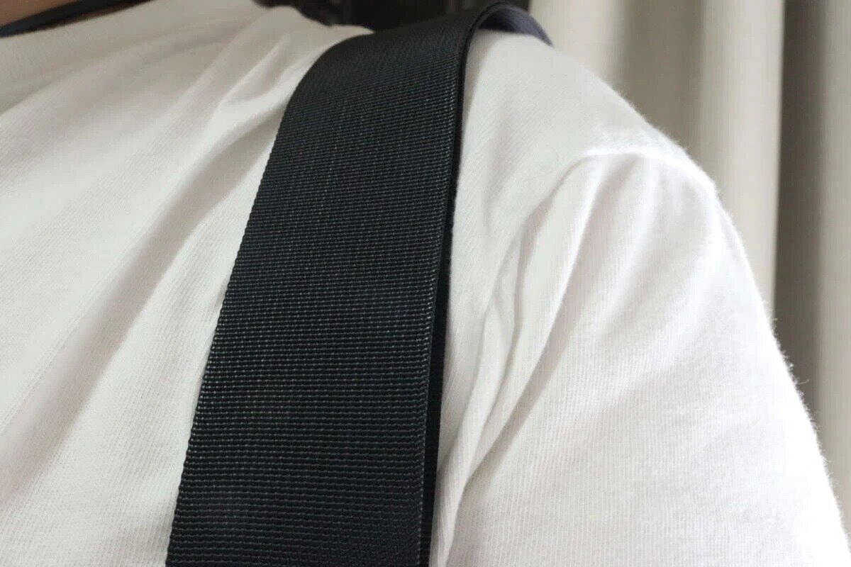 一個身穿白色T恤的人肩上背著黑色單肩包帶。 白いTシャツを着た人の肩に黒いショルダーバッグストラップがかかっている