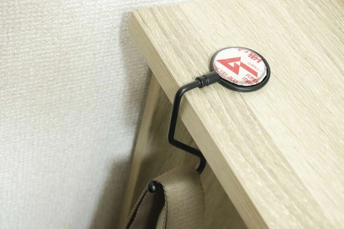 木紋桌邊緣安裝了一個黑色掛鉤,下面掛著一個包包。 黒いバッグフックが木目調のテーブルの縁に設置され、下にバッグが掛けられている