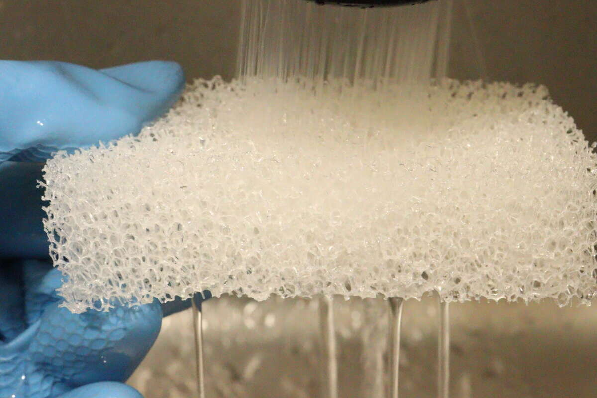 一隻戴著藍色橡膠手套的手正在往一塊能很好地吸水的海綿上倒水。 青いゴム手袋をはめた手が、水キレの良いスポンジに水を流している様子