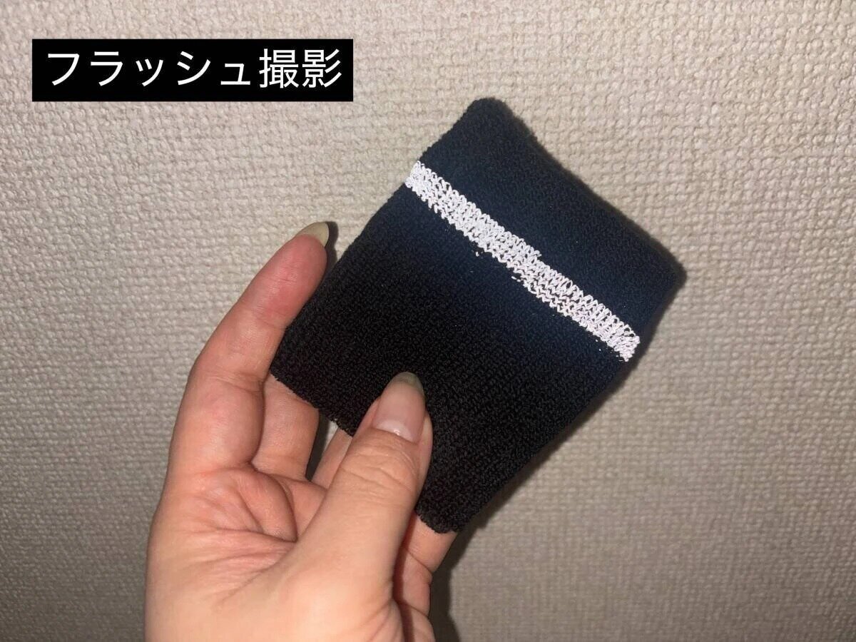 女人手中拿著的黑色腕帶的反光部分在閃光燈下閃著白光。 女性の手が持っている黒いリストバンドのリフレクター部分がフラッシュで白く光っている様子