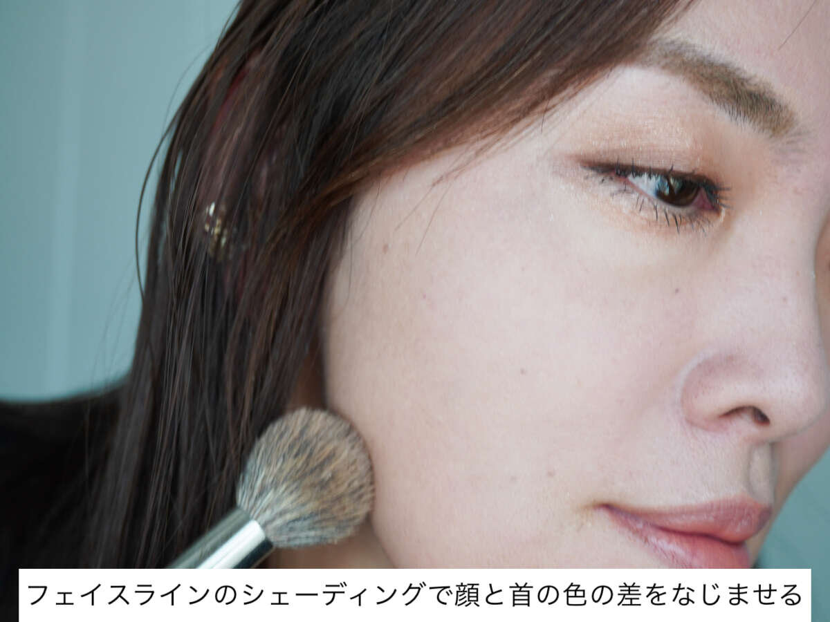 40代女性がフェイスラインにシェーディングブラシでパウダーを塗布している。