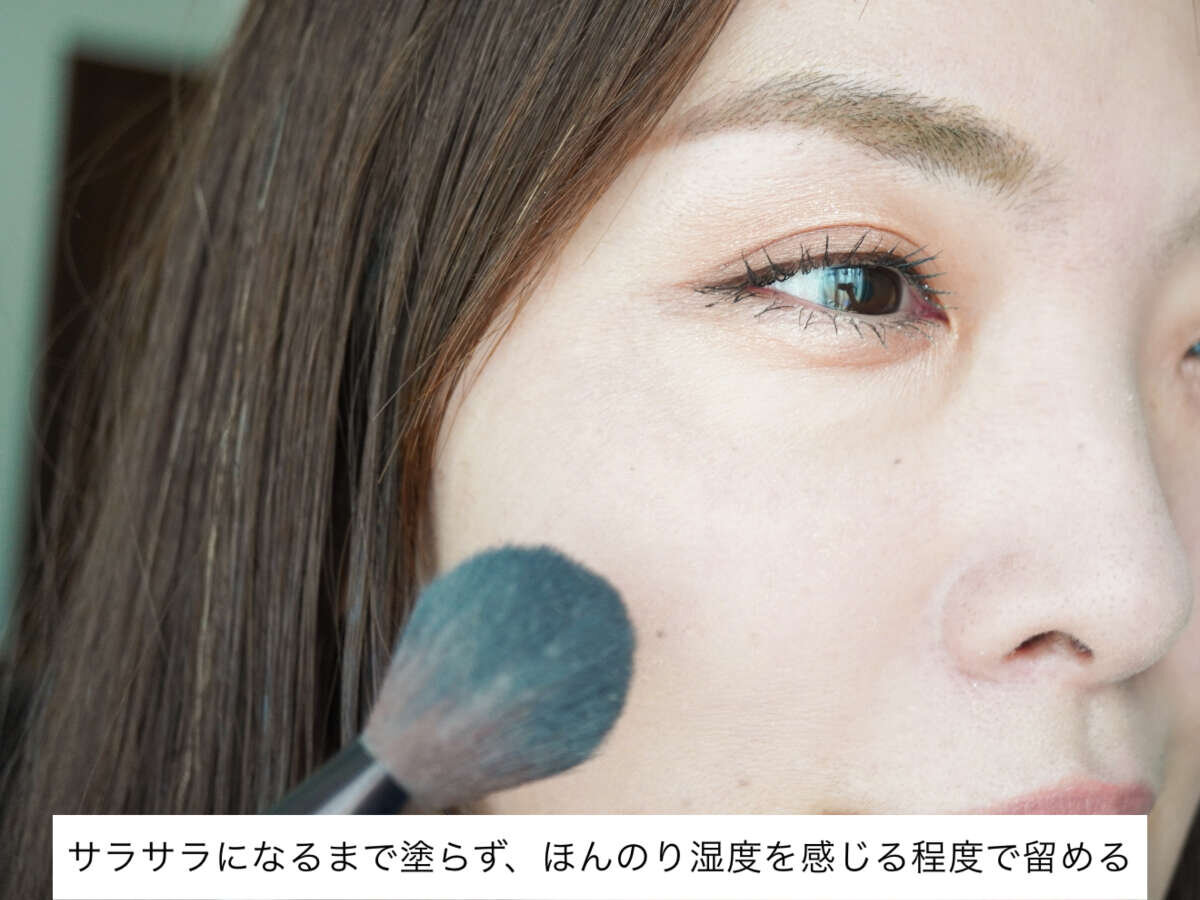 40代女性が頬にフェイスパウダーをブラシで軽く塗布している。