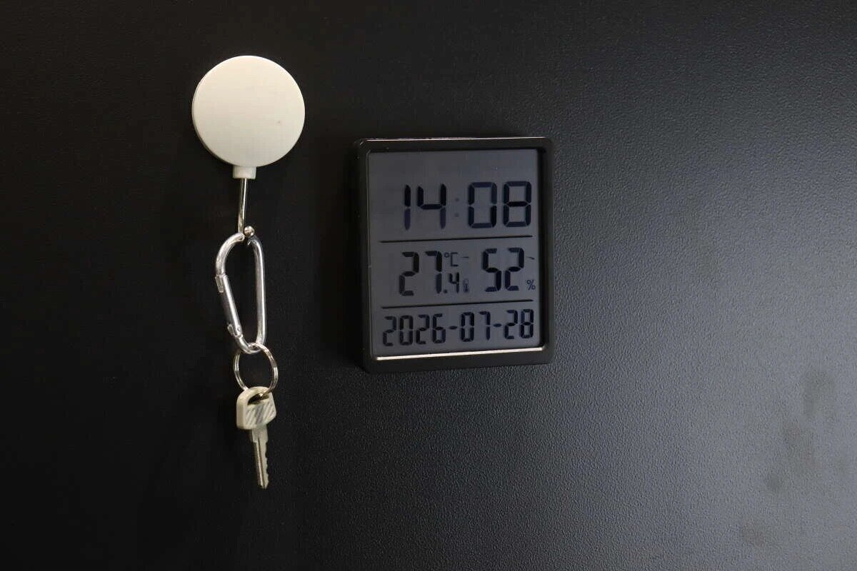 一個用磁鐵吸附在黑色牆上的電子鐘,旁邊掛著一把鑰匙。 黒い壁にマグネットで設置されたデジタル時計と、隣に吊るされた鍵