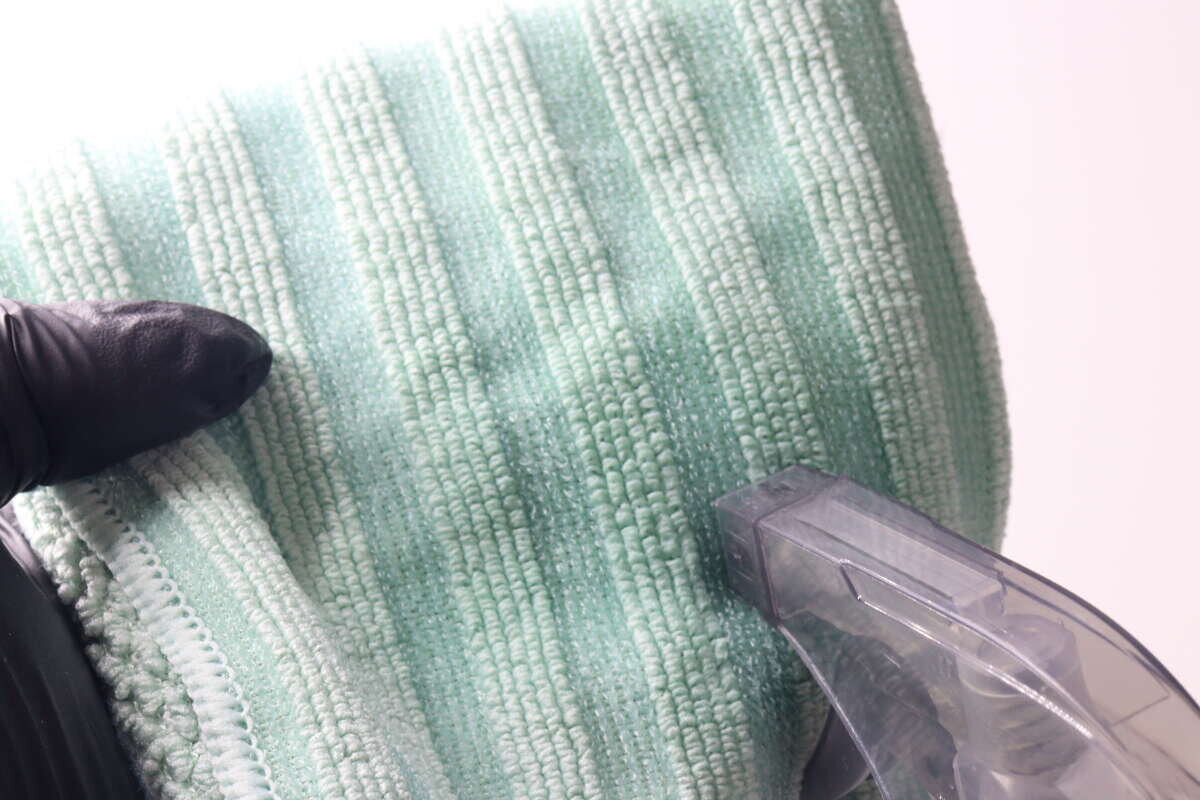 液體正從噴霧瓶噴灑到一塊綠色超細纖維布上。 スプレー容器から緑色のマイクロファイバークロスに液を吹き付けている状態