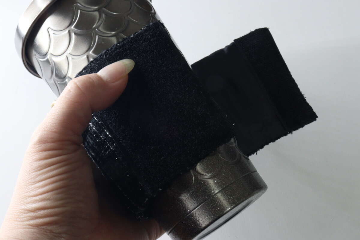 一隻手將杯套套在玻璃杯上,並用魔鬼氈固定。 タンブラーにカップスリーブを巻き付けて面ファスナーで留めている手元