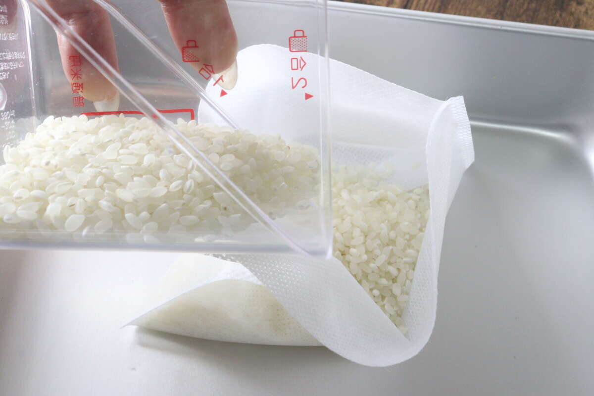將生白米從量杯轉移到不織布煮飯袋中的過程。 計量カップから白い生米を不織布の炊飯袋へ入れている工程