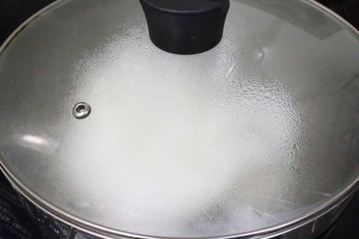 一張俯拍照片,顯示米飯在有玻璃蓋的鍋子裡蒸騰。 鍋にガラスのフタをしてお米を蒸らしている俯瞰写真