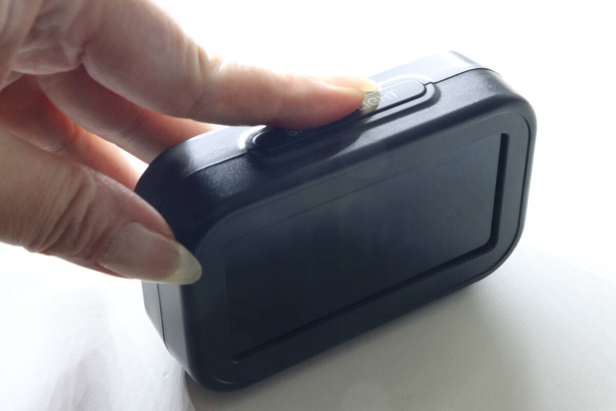時計の上部にあるスヌーズとライトのボタンを指で押している様子