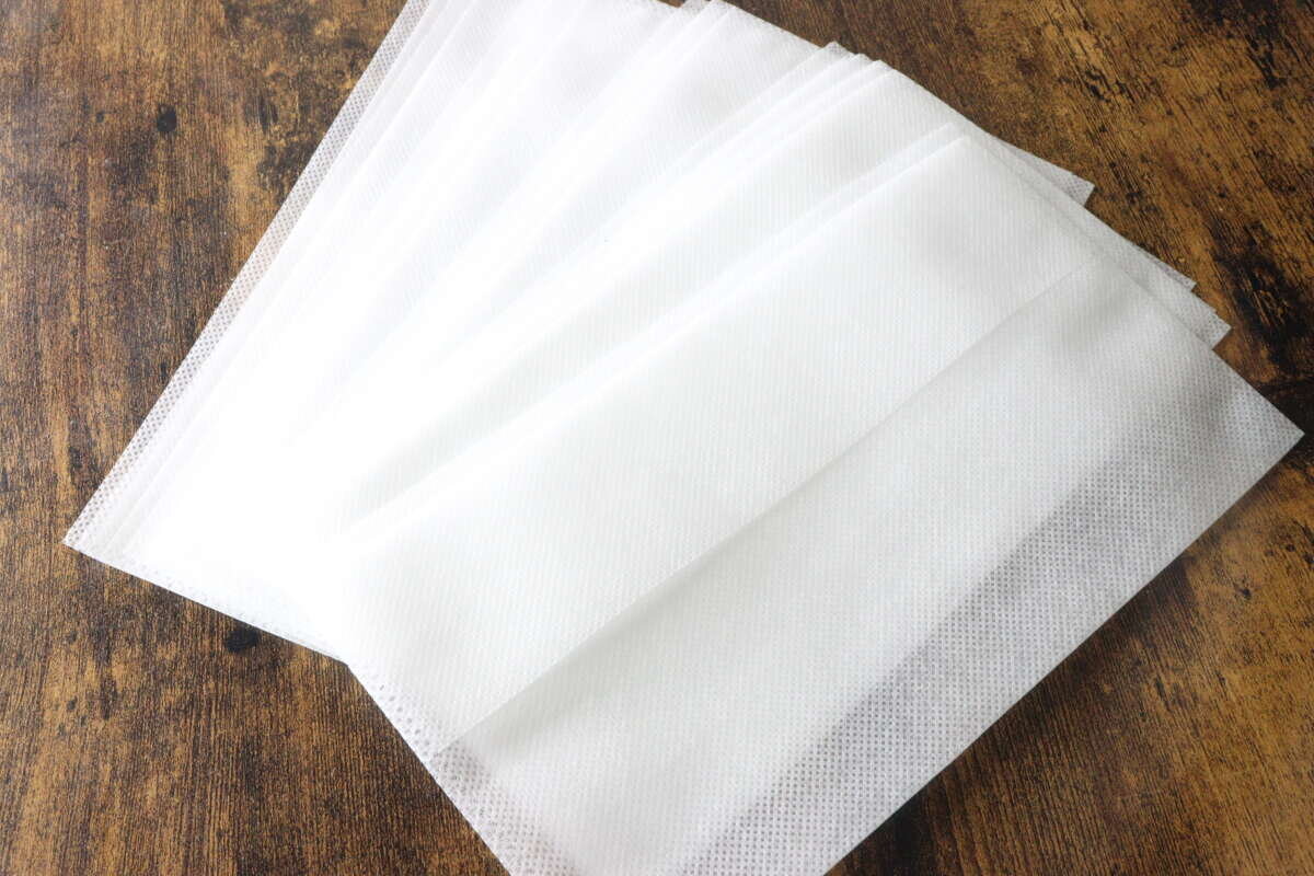 一包10個白色不織布煮飯袋堆放在木架上。 木目の台の上に重ねて置かれた10枚入りの白い不織布製炊飯袋