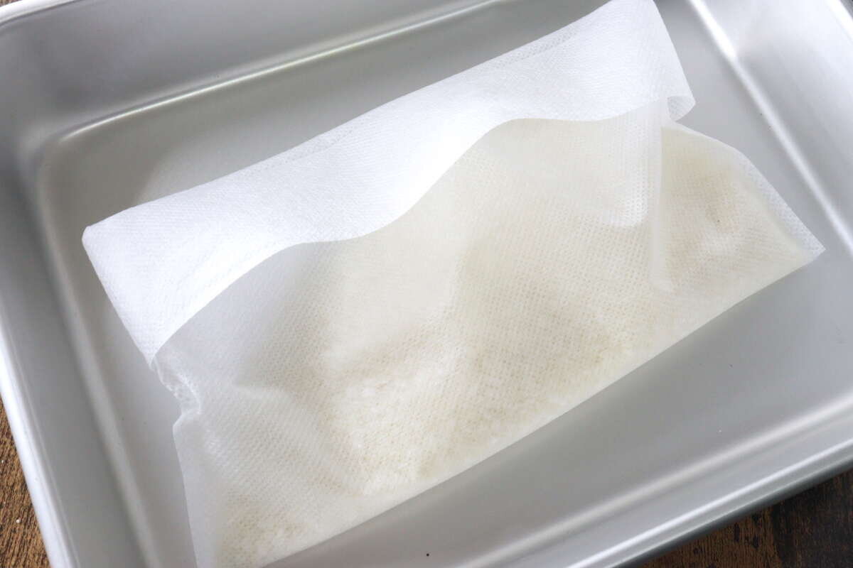 一張俯拍照片顯示,一個電飯煲袋放在托盤上,袋口折疊起來以防止米飯溢出。 口を折り返して中身が出ないようにした炊飯袋をトレーに置いた俯瞰写真