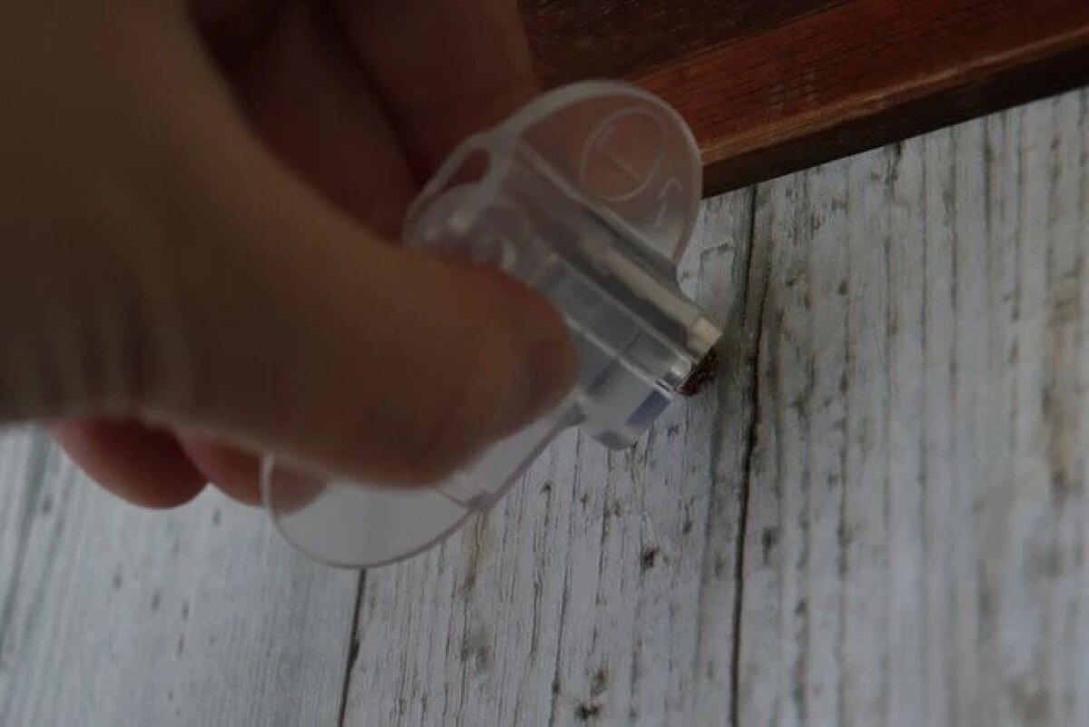 圖片顯示有人將蓋子固定在牆上的木釘上,然後用手將其取下。 壁の木部に取り付けられたおれくぎにカバーをセットして手で回して外している様子