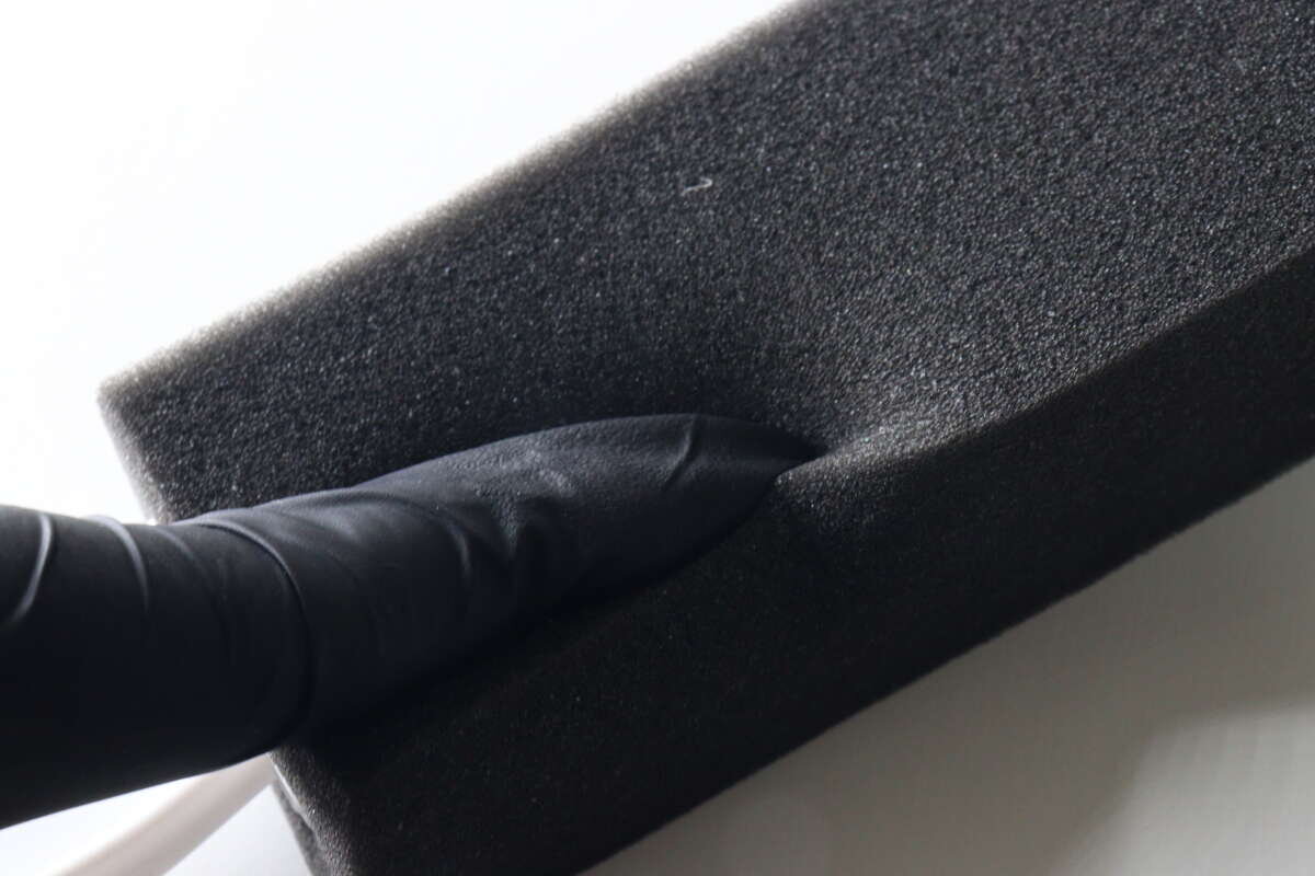 這個人正戴著手套,用手指感受海綿柔軟的質地。 黒い手袋をした指でやわらかなスポンジの素材感を確認している様子
