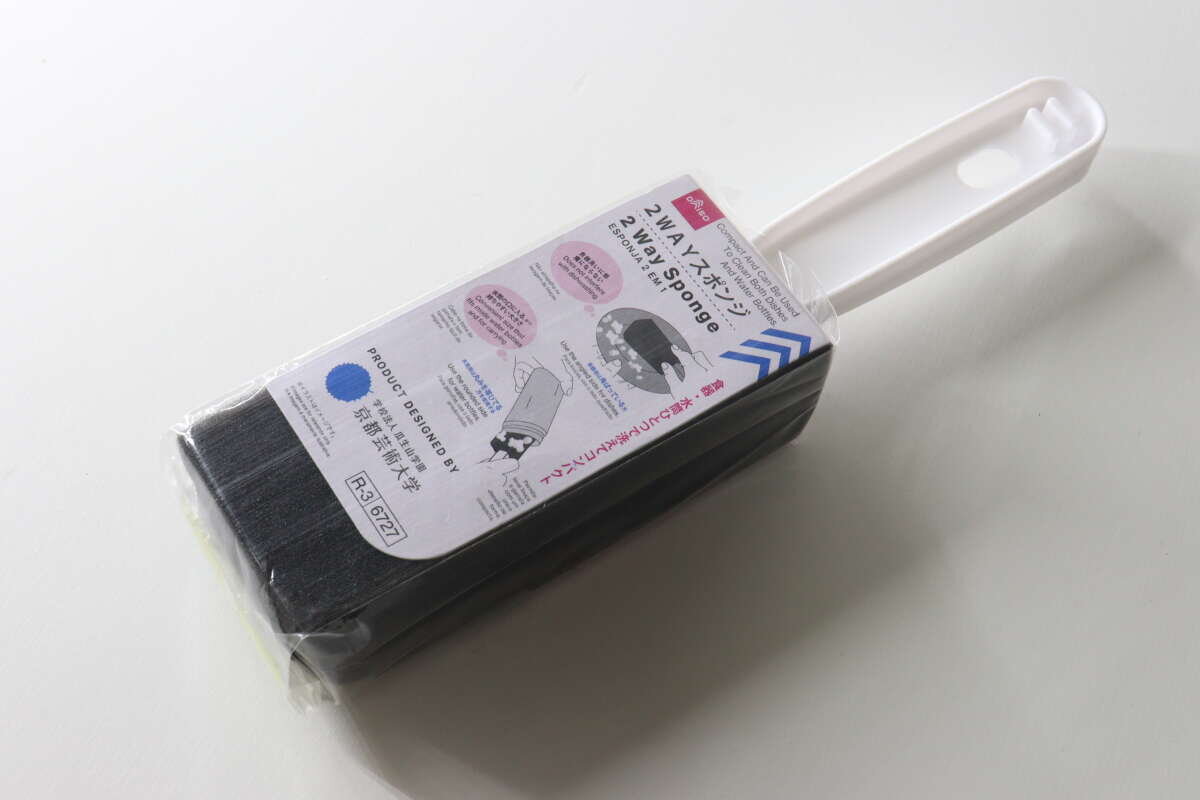 從側面拍攝的大創雙面海綿的全身照,海綿裝在白色包裝盒內。 白いパッケージに入ったダイソーの2WAYスポンジを斜めから捉えた全体写真