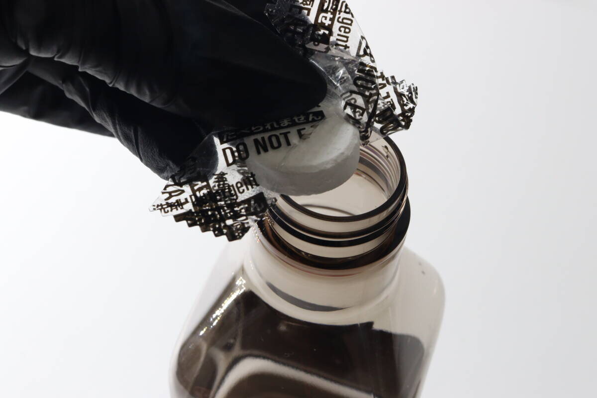一名戴著黑色手套的人將一片藥片放入噴霧瓶的瓶口。 黒い手袋をした手でスプレー容器の口に錠剤を入れている様子