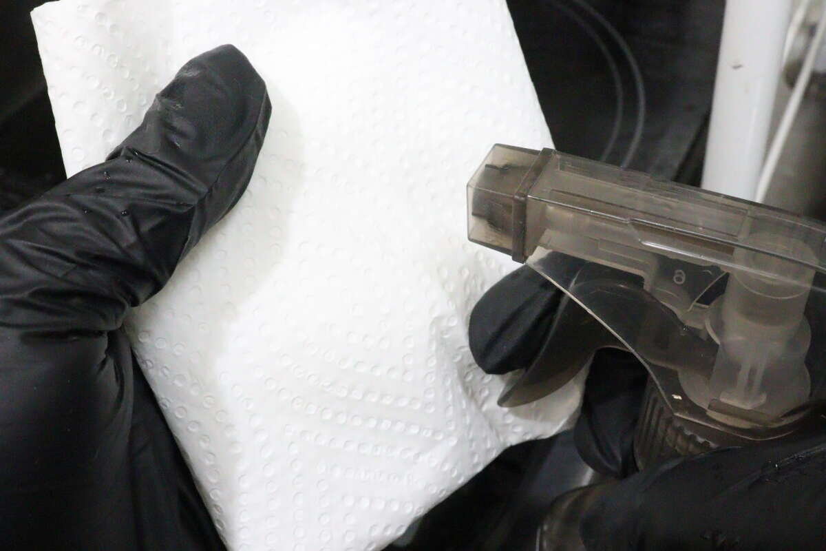 一名戴著黑色手套的人正用噴霧瓶對著一張紙巾噴灑。 黒い手袋をした手でスプレー容器をキッチンペーパーに向けている様子