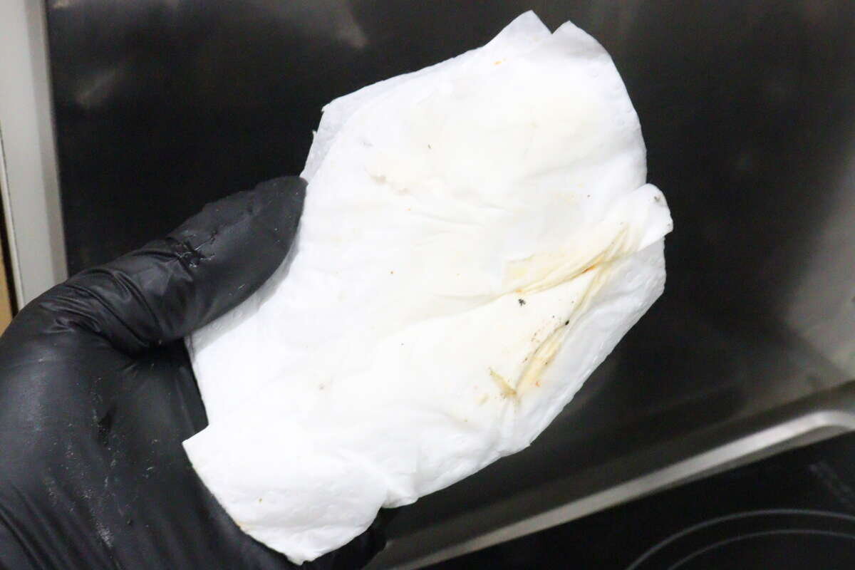 一隻手舉著一張泛黃的廚房紙巾,剛剛擦掉了污垢。 汚れを拭き取ったあとの黄色っぽくなったキッチンペーパーを掲げる手元