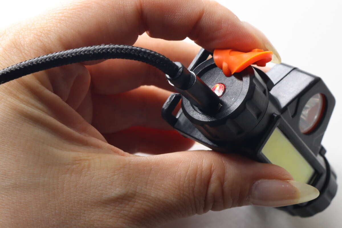 圖片顯示,透過將 USB 連接線插入黑色機身上的連接埠來為裝置充電。 黒い本体の端子にUSBケーブルを挿して充電している様子