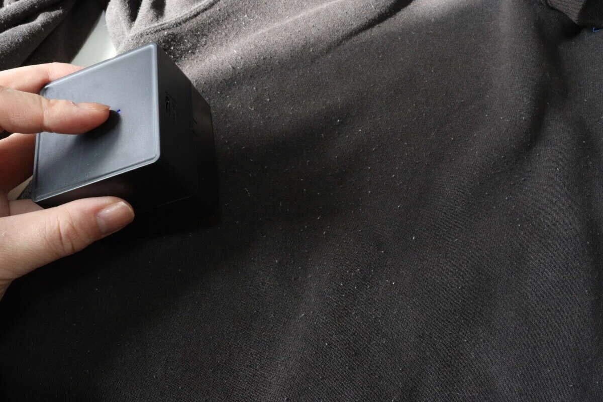 圖片顯示有人拿著電動除毛器對著黑色衣服,按下電源按鈕。 黒い衣類の上に電動毛玉取りを当てて電源ボタンを押している様子