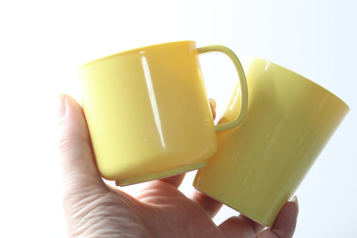 一隻手掌中放著一個黃色馬克杯和一個杯子。 手のひらに黄色いマグカップとカップを乗せている状態