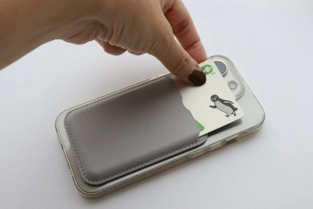 一隻手將卡片從智慧型手機背面的卡片套中取出並放入。 スマホの背面に装着したカードホルダーからカードを出し入れしている手元
