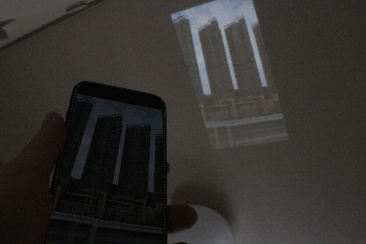 一間昏暗的房間,用投影機將智慧型手機螢幕投射到牆上。 スマホの画面をプロジェクターで壁に投影している暗い部屋の様子