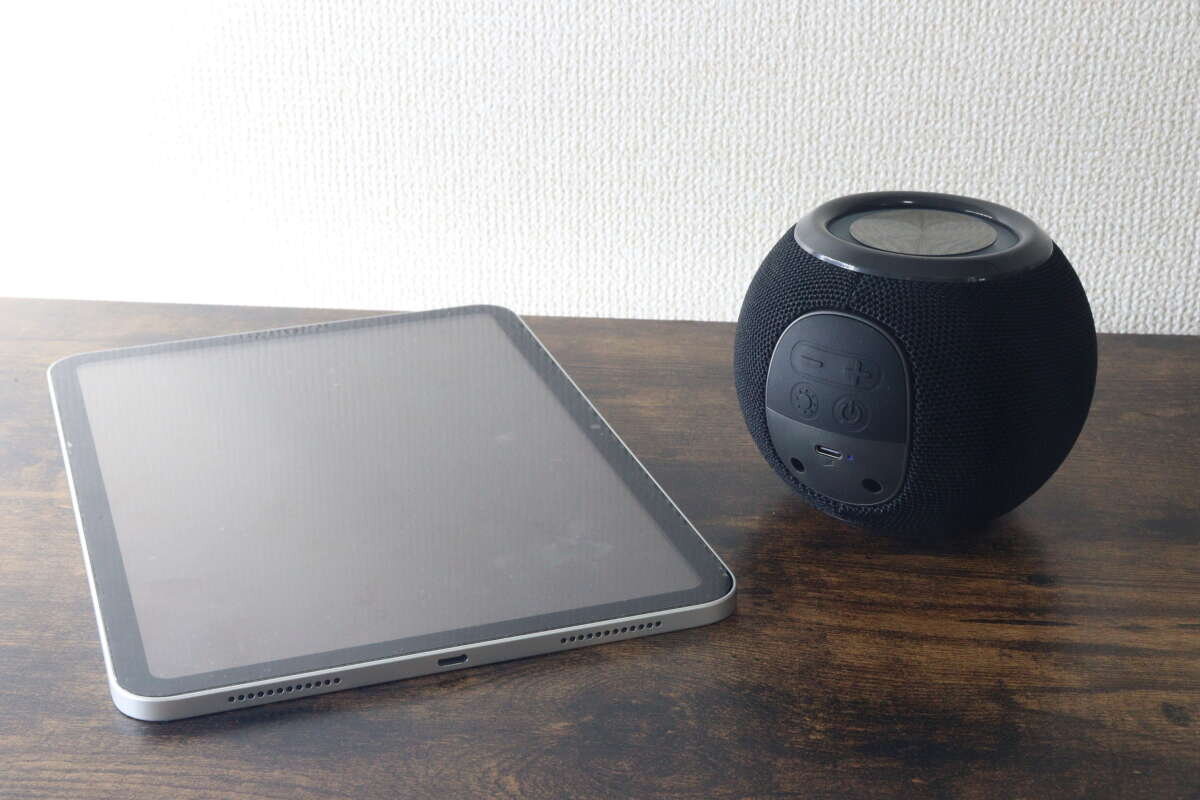 一台平板電腦和一個黑色球形揚聲器並排放置。 タブレット端末と黒いボール形スピーカーを並べて置いている様子
