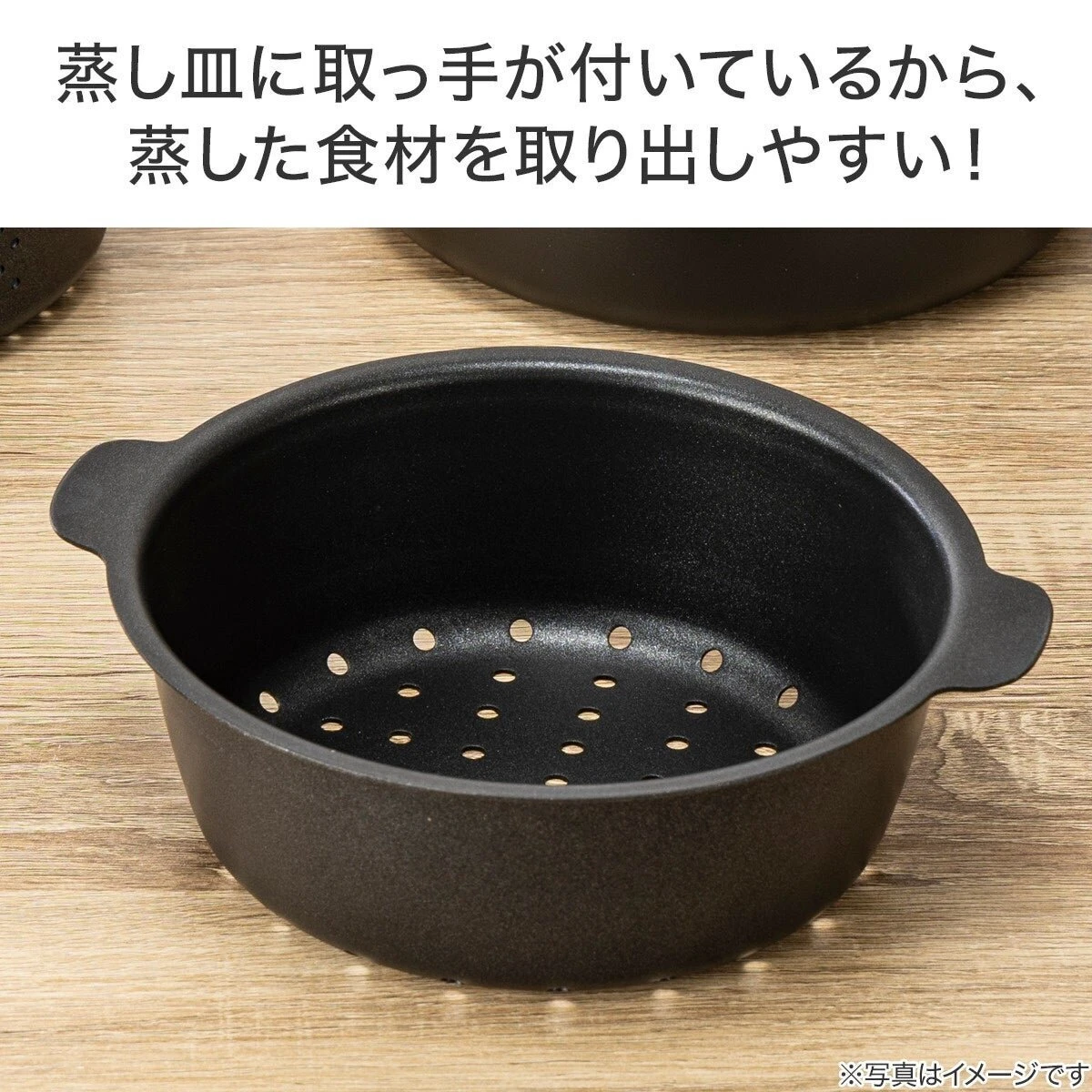 取っ手が付いた黒い蒸し皿が木製テーブルに置かれている 取っ手が付いた黒い蒸し皿が木製テーブルに置かれている