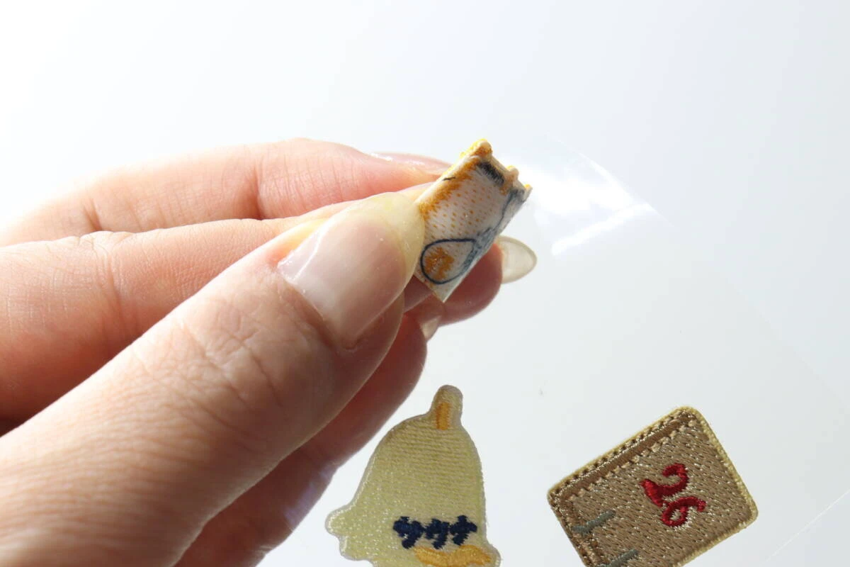 指でサウナモチーフのワッペンを透明なシートから剥がしている手元